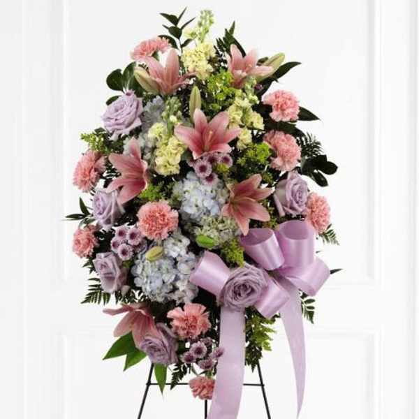 Standing floral spray with pink lilies, lavender roses, and a purple ribbon