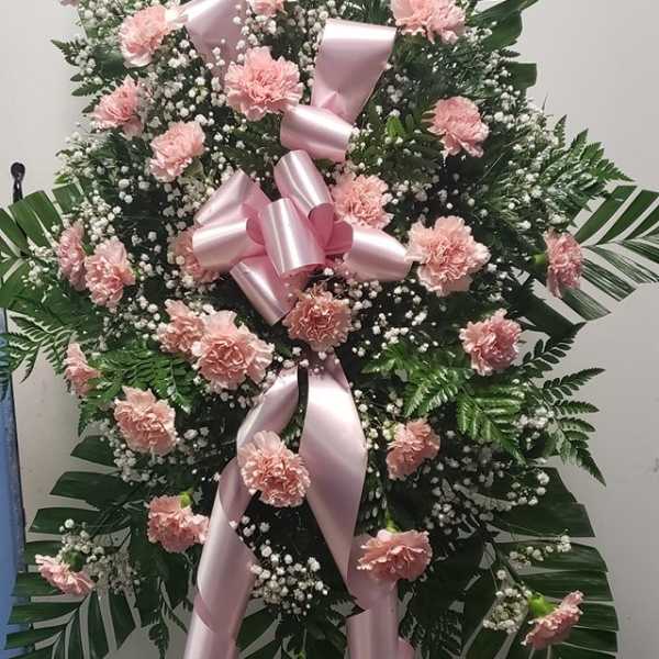 Pink carnation standing spray with a large pink ribbon on an easel