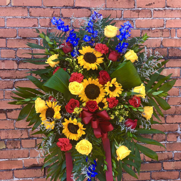 Standing floral spray with sunflowers, roses, and blue orchids on an easel