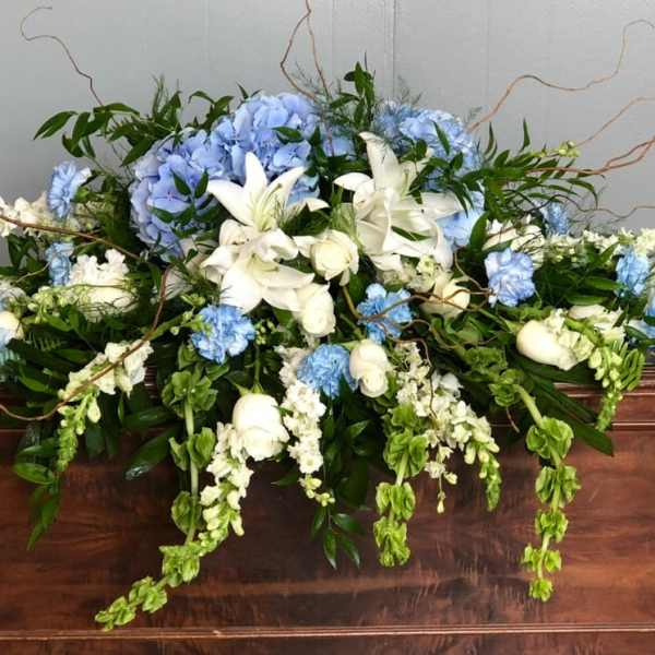 Large blue and white floral arrangement on a wooden casket