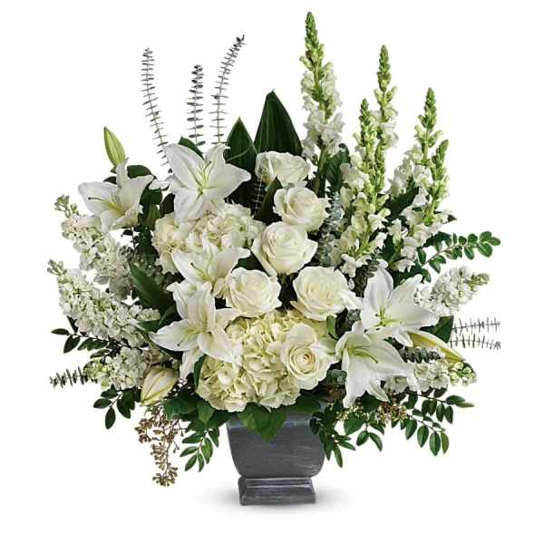 Tall white arrangement of lilies, roses, hydrangeas, and snapdragons in a gray pedestal vase