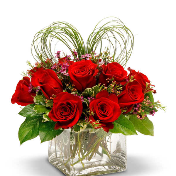 Red roses arranged in a clear square vase with looping grass accents