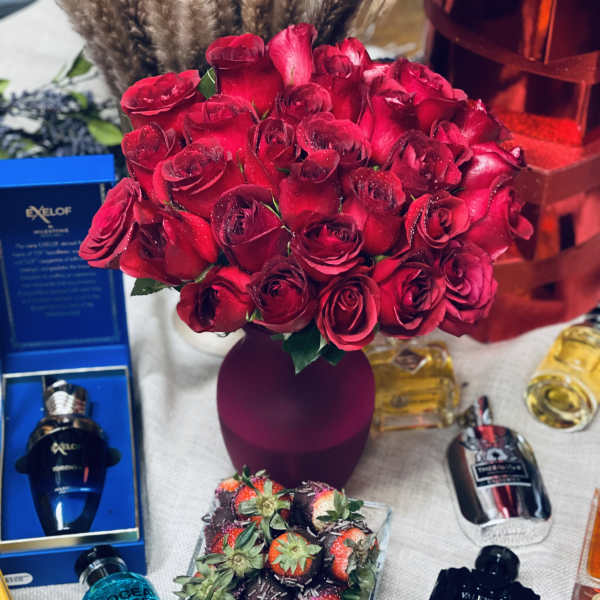 Bouquet of red roses in a purple vase with perfume bottles and chocolate-covered strawberries