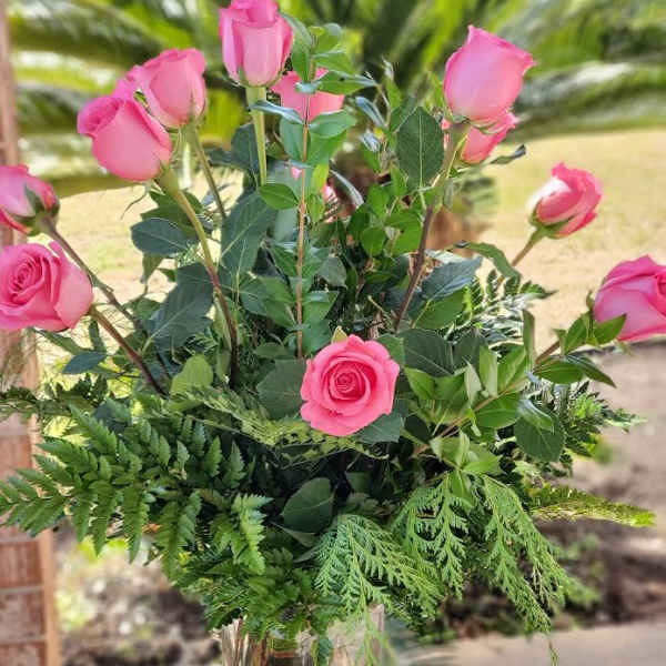 Tall arrangement of pink roses with lush greenery in a clear glass vase