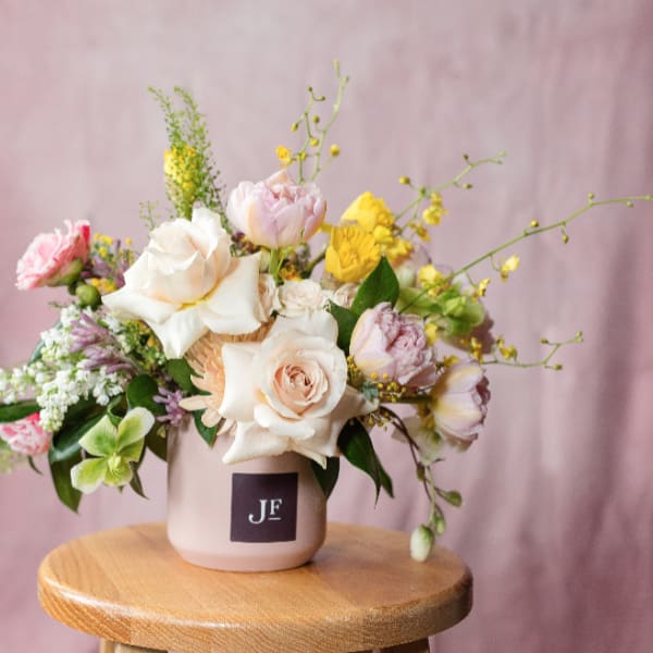 Pastel flower arrangement in a blush vase on a wooden stool