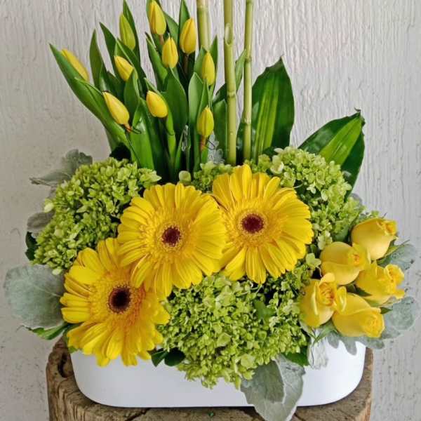 Yellow gerberas and tulips arranged with bamboo in a white container