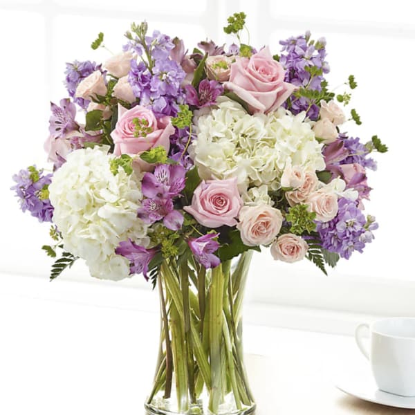Bouquet of pink roses, white hydrangeas, and purple flowers in a glass vase