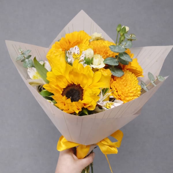 Yellow bouquet with a sunflower and white accent flowers wrapped in paper
