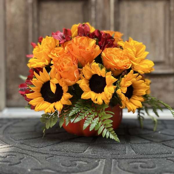 Bouquet of sunflowers, orange roses, and red flowers in a red container