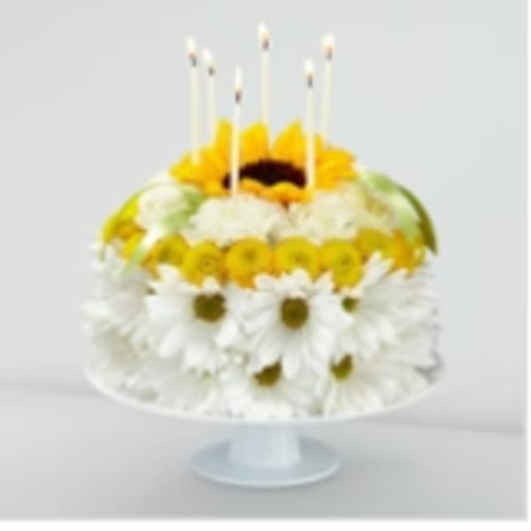 Round floral cake with white daisies and yellow blooms topped by candles