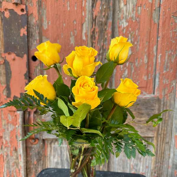 Yellow roses in a clear glass vase with greenery