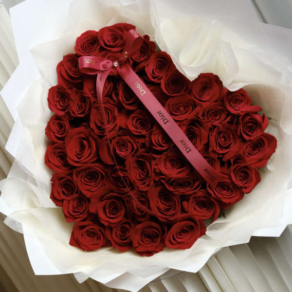 Large bouquet of red roses wrapped in white paper with a pink ribbon