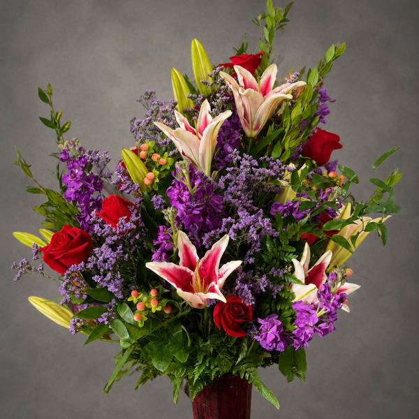 Tall bouquet of red roses and pink lilies in a red vase