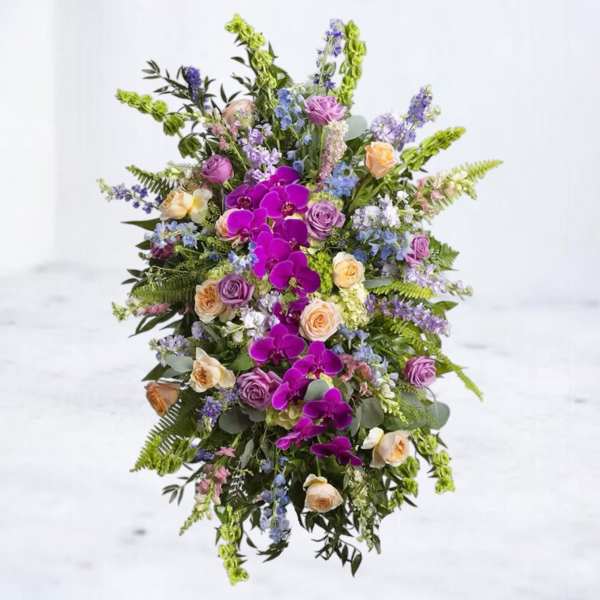 Tall spray of bright purple orchids, pastel roses, and blue flowers in an elongated oval design.