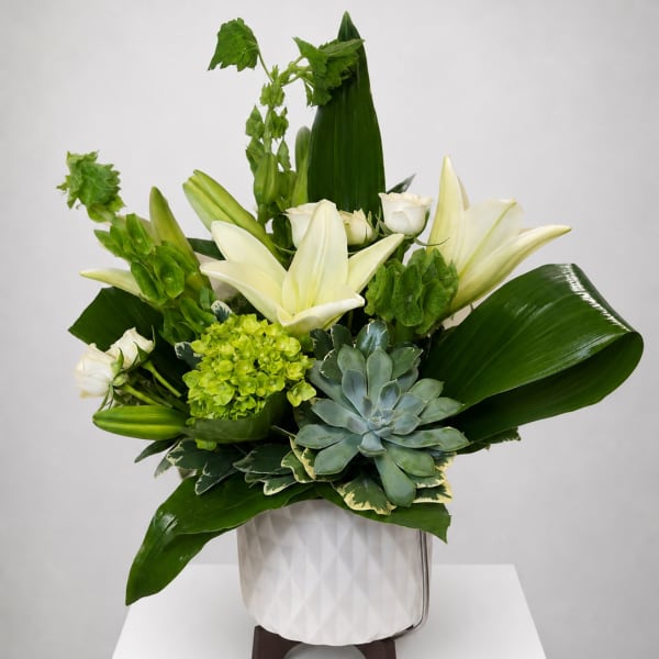 White lilies and green flowers in a white vase with a succulent accent