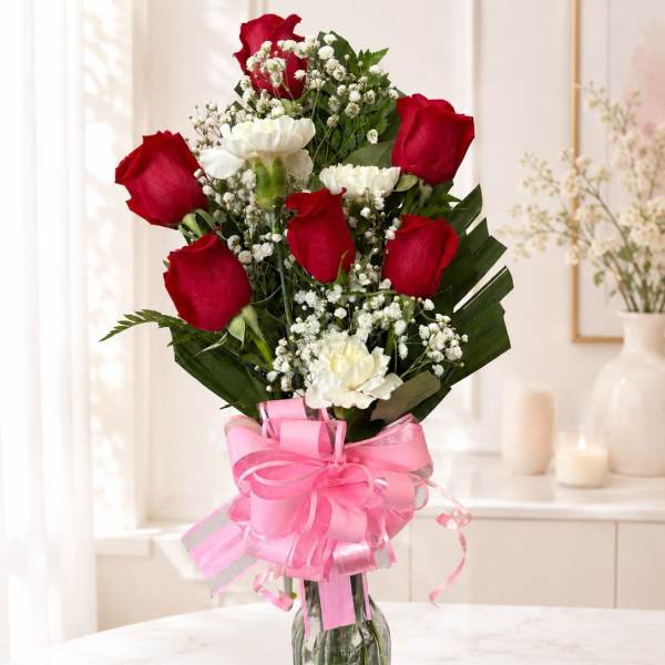Red roses and white carnations in a glass vase with a pink ribbon