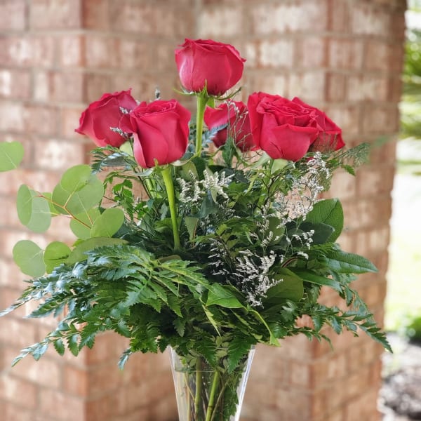 Tall vase arrangement of red roses with mixed greenery