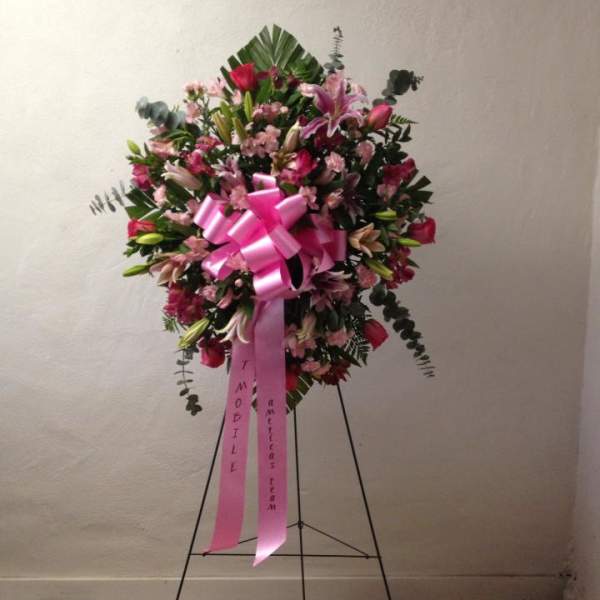 Pink and white funeral spray on a stand with a large pink ribbon