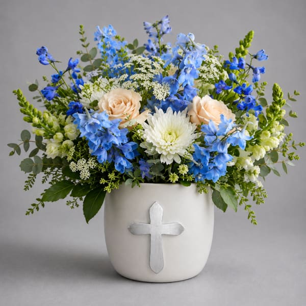 Blue and white floral arrangement in a white vase with a cross emblem