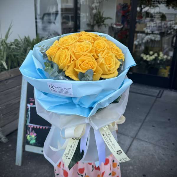 Bouquet of yellow roses wrapped in blue paper with a white ribbon