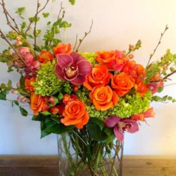Orange roses and purple orchids in a clear glass vase