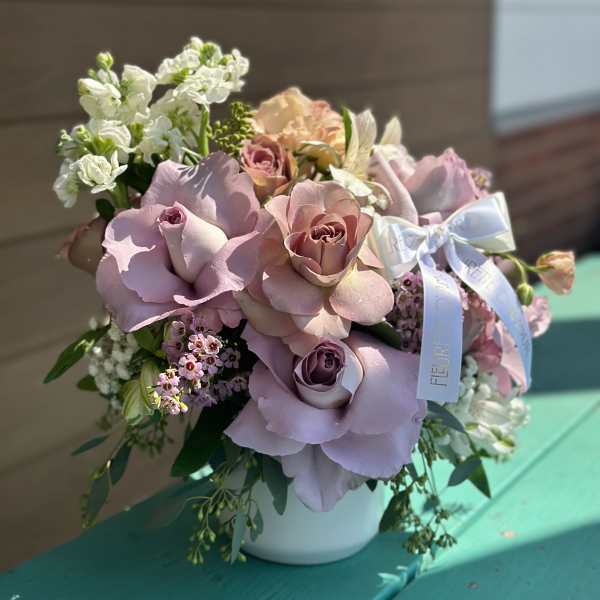 Pink and lavender rose bouquet in a white vase with a ribbon