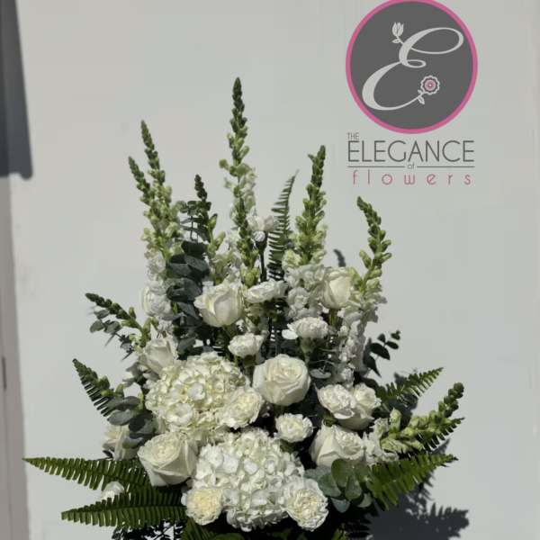 White floral arrangement in a vase with tall greenery and roses