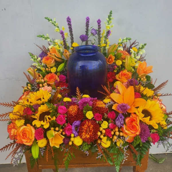 Colorful floral arrangement around a blue urn on a wooden stand