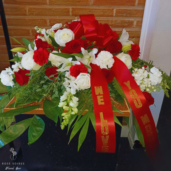 Red and white rose arrangement with lilies and ribbons on a table