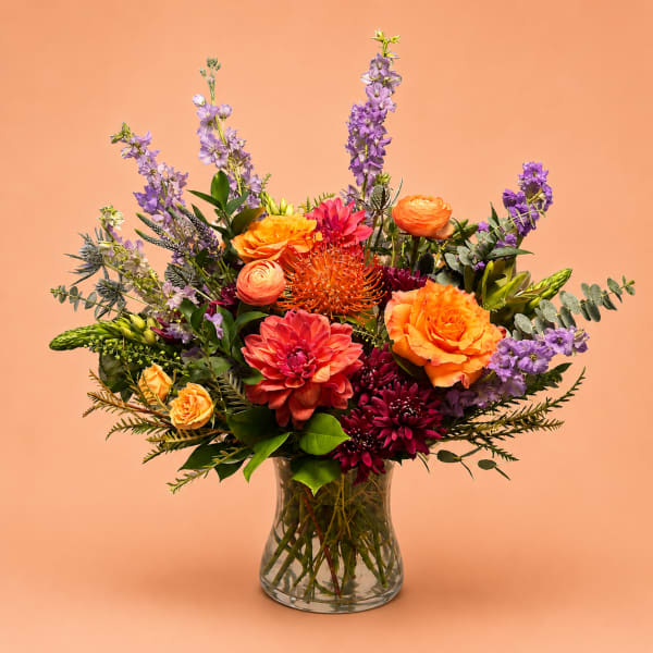 Mixed bouquet of orange, pink, and purple flowers in a clear glass vase
