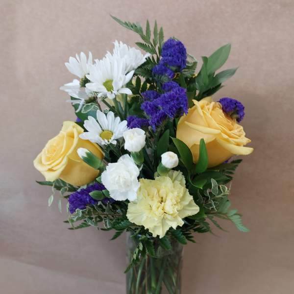 Bouquet of yellow roses, white daisies, and purple filler in a glass vase