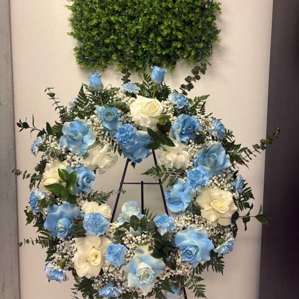 Blue and white rose wreath on a stand beneath a green foliage panel