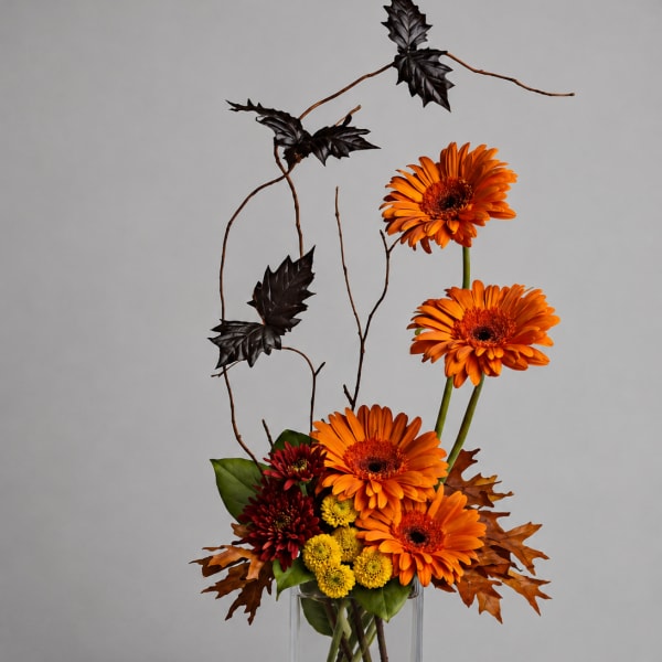 Orange gerbera daisies in a clear glass vase with autumn leaves