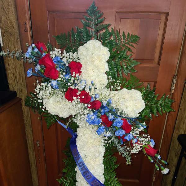 Cross-shaped floral tribute with white carnations, red roses, and blue flowers