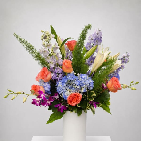 Colorful mixed bouquet in a white vase with roses, lilies, hydrangeas, and orchids