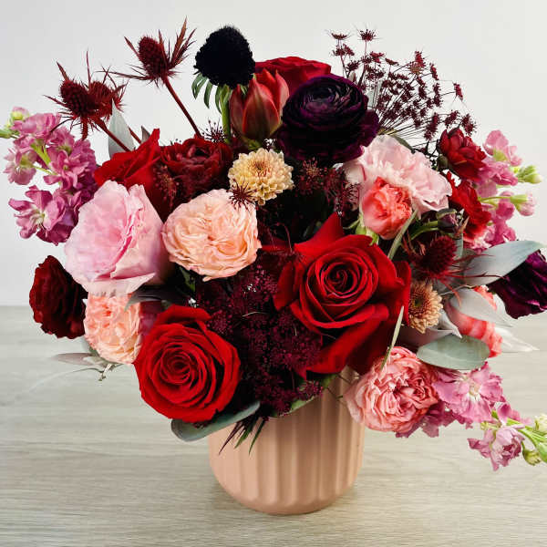 Mixed bouquet of red, pink, and burgundy flowers in a blush vase