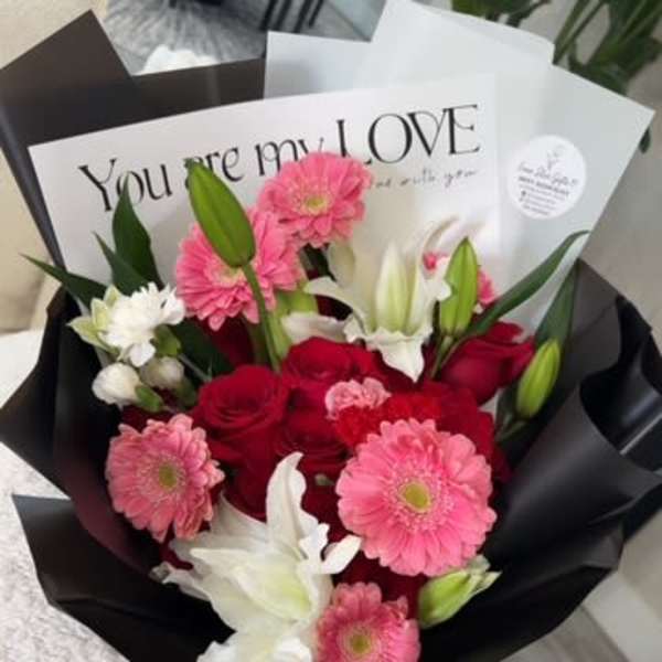 Bouquet of pink gerbera daisies, red roses, and white lilies in black wrap