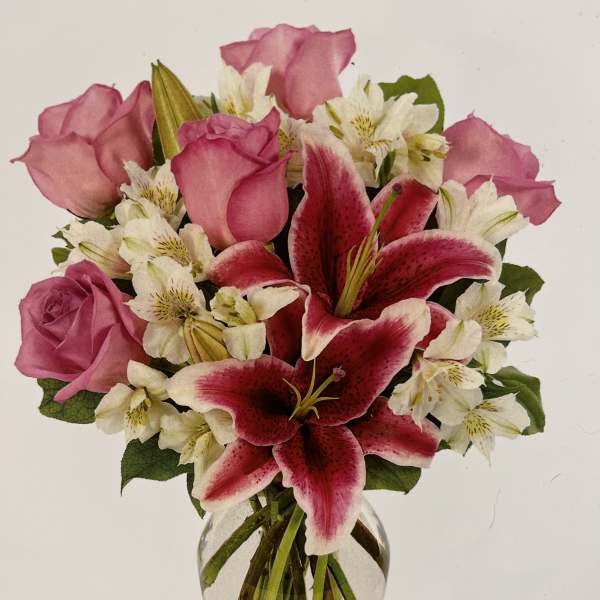 Clear glass vase with pink roses, pink lilies, and white alstroemeria in a mixed bouquet