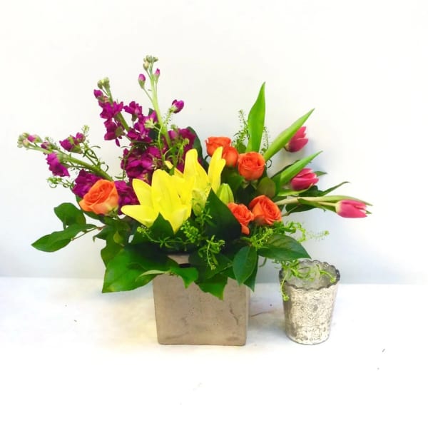 Colorful bouquet in a square vase with roses, tulips, and lilies