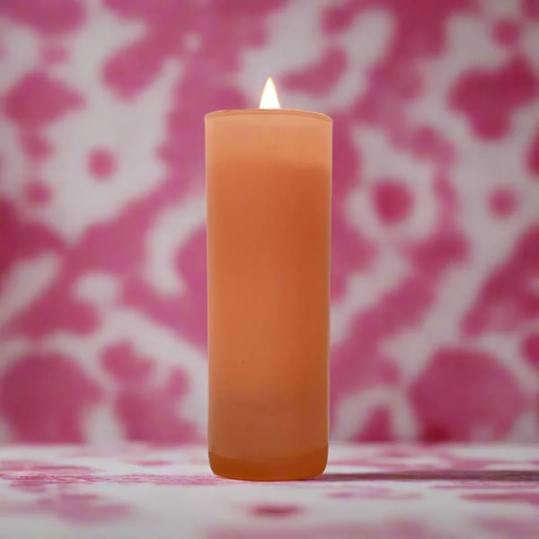 Lit orange pillar candle against a pink patterned background
