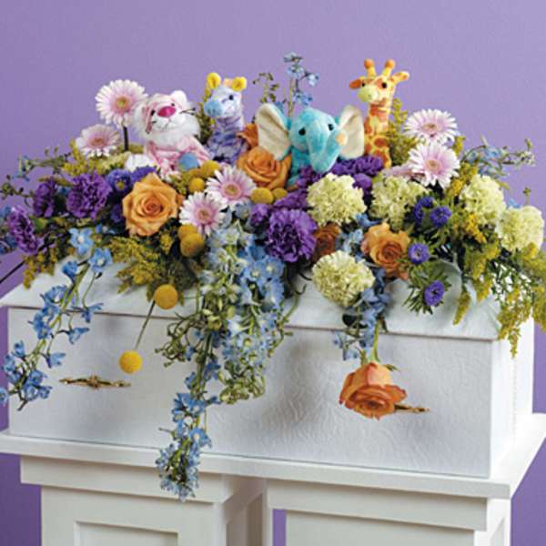 Colorful floral arrangement with plush animals on a white casket