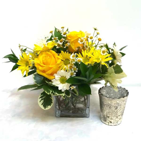 Yellow roses and daisies in a glass vase beside a silver votive holder