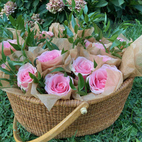 Pink roses in brown paper inside a wicker basket