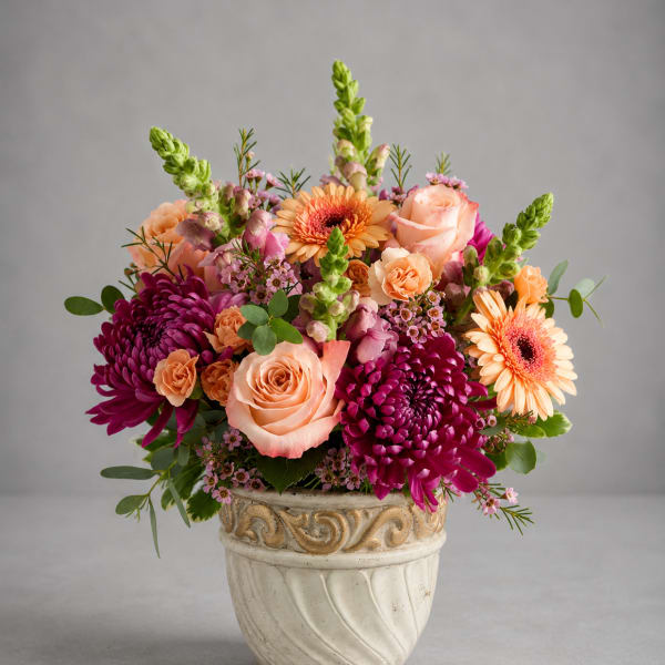 Mixed bouquet of peach, pink, and purple flowers in a decorative ceramic pot