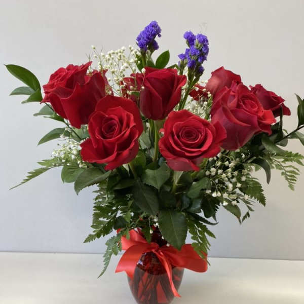 Red roses with white and purple filler flowers in a red vase with a red ribbon bow