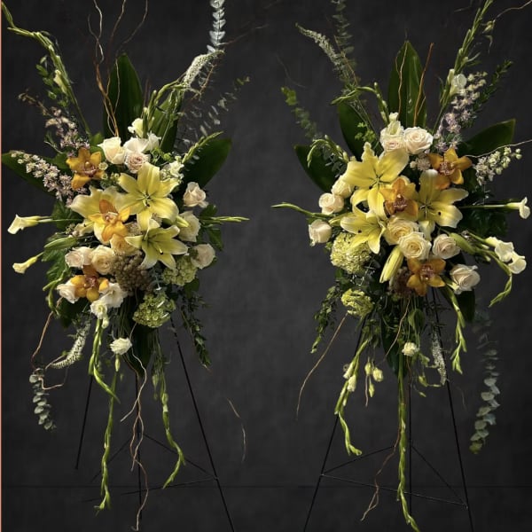 Two tall floral sprays with yellow lilies and white roses on stands