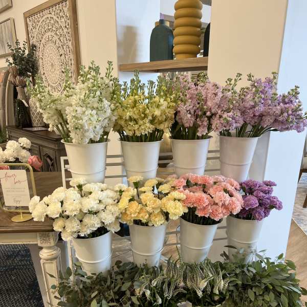 Rows of pastel flowers in white buckets on a display stand