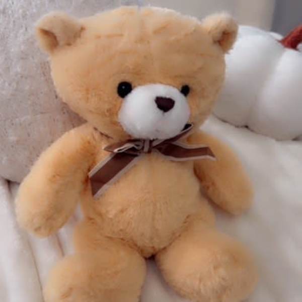 Plush teddy bear with a ribbon bow sitting on a bed