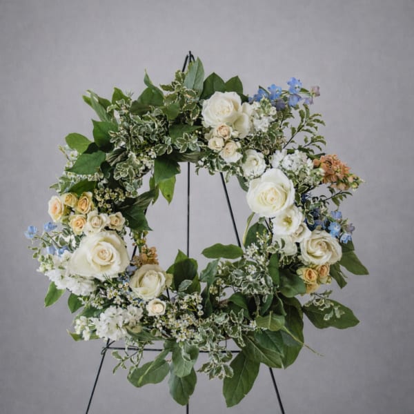 Floral wreath with white roses, blue flowers, and greenery on a stand