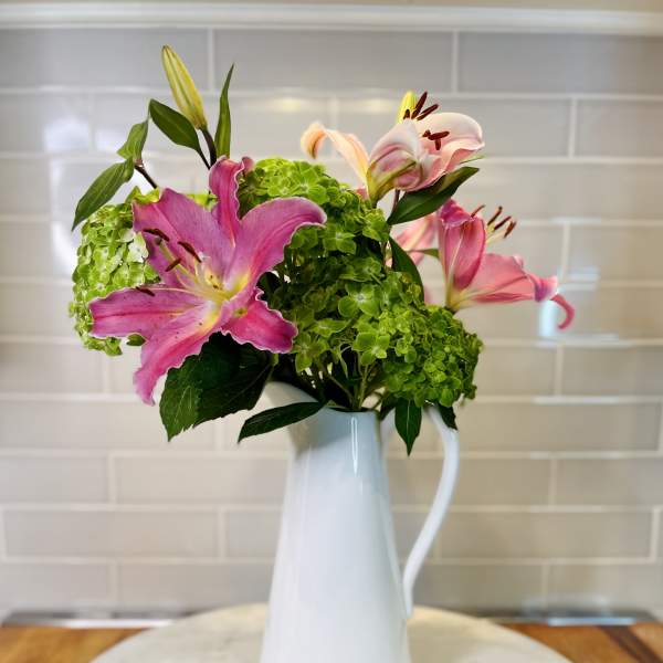 Pink lilies and green hydrangeas arranged in a white pitcher vase
